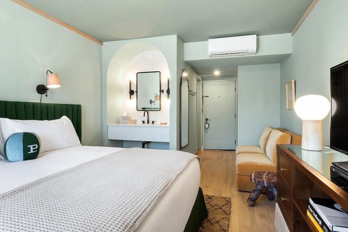Une chambre d’hôtel comprenant un lit, une coiffeuse avec un miroir, une télévision et un canapé.