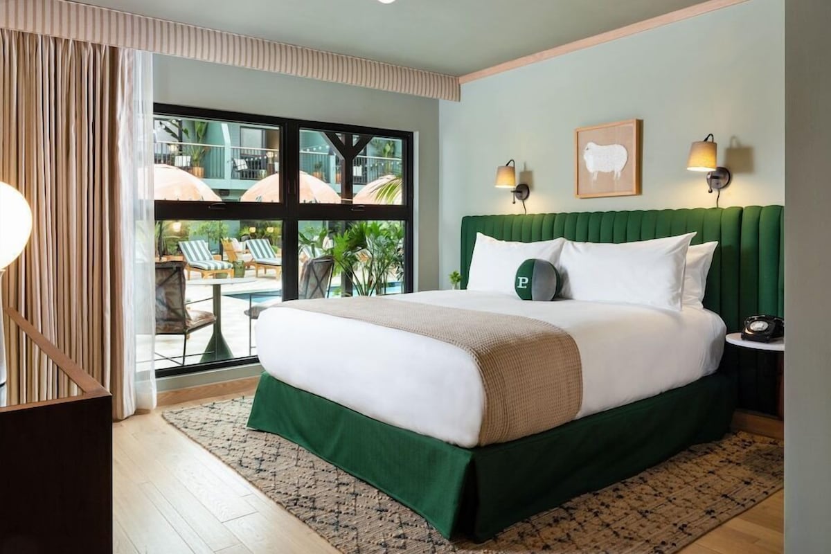 Une chambre d’hôtel avec un grand lit, une vue sur la piscine extérieure et deux lampes fixées au mur.