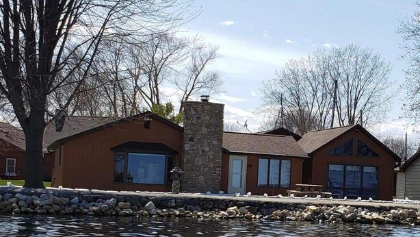 Un chalet au bord du lac, doté d’une cheminée en pierre, de grandes fenêtres et d’une jetée qui s’avance sur l’eau.