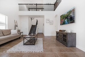 A spacious living area with a staircase leading to an upper floor, a large painting on the wall, and a modern coffee table.