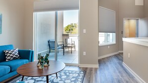Ein modernes Wohnzimmer mit einem blauen Sofa, einem Holztisch und einer Glastür, die auf einen Balkon führt.