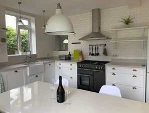 Een moderne keuken met witte kasten, een centraal eiland, een fornuis en hangend keukengerei.