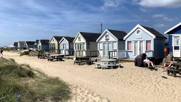 A row of beach cottages with outdoor seating and a sandy beach in the background.