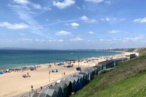 Una playa con una hilera de cabañas azules a lo largo de la orilla, arena y el mar al fondo.