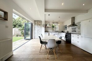 Een moderne keuken met witte kasten, een centraal eiland en een eethoek met een glazen deur naar een tuin.