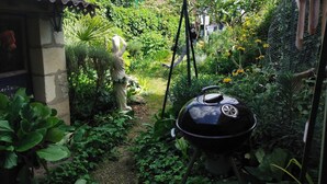 Un jardín con una estatua, una parrilla y una casa al fondo.
