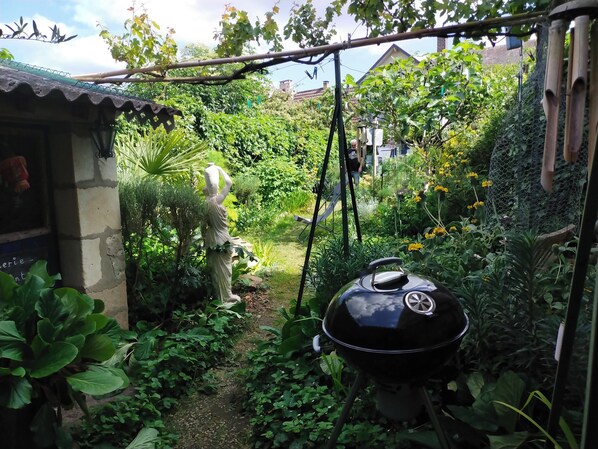 A garden with a statue, a grill, and a house in the background.