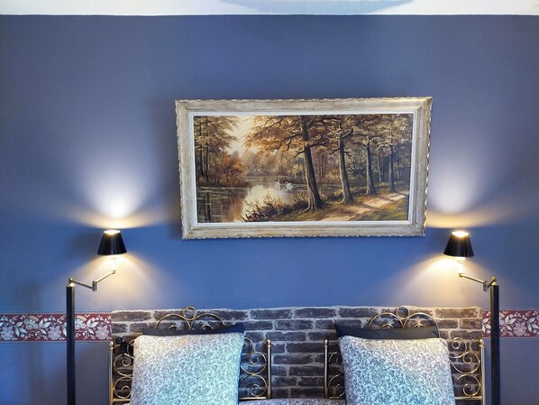 Une chambre à coucher avec une tête de lit en briques, un tableau encadré représentant une scène de forêt et deux lampes de chevet.