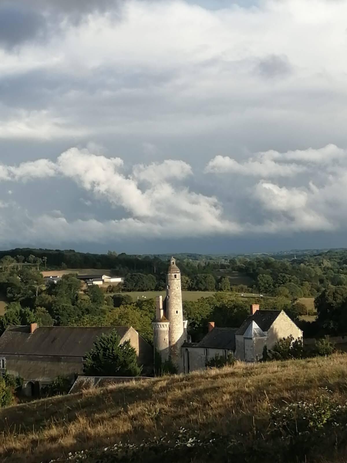 Uma torre histórica rodeada por edifícios tradicionais, com colinas ondulantes e um céu nublado ao fundo.