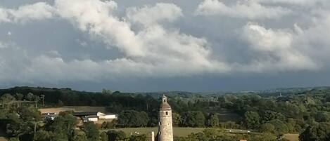Uma torre histórica rodeada por edifícios tradicionais, com colinas ondulantes e um céu nublado ao fundo.