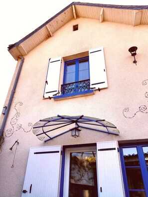Un bâtiment doté d’un toit à deux versants, d’une fenêtre avec des volets bleus, d’un balcon décoratif et d’une lanterne fixée au mur.