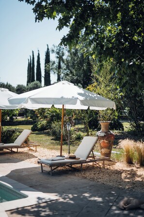 A poolside area with lounge chairs, umbrellas, and a decorative vase. - Mas in Provence at Domaine du Printemps (Monteux)