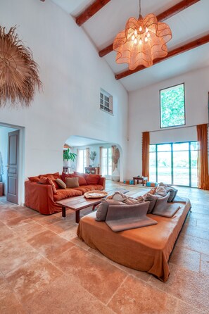A spacious living area with a large sofa set, a hanging light fixture, and a view through an arched doorway. - Mas in Provence at Domaine du Printemps (Monteux)