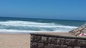 Une plage où les vagues se brisent sur le rivage, un mur de pierres et une tente rouge et blanche.