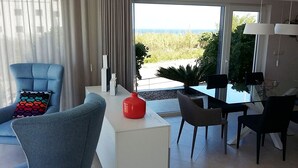 Un salon moderne avec un fauteuil bleu, une table d’appoint blanche et un coin repas comprenant une table et des chaises en verre.