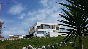 Un immeuble résidentiel moderne à plusieurs étages, doté de balcons, situé sur une colline verdoyante sous un ciel dégagé.