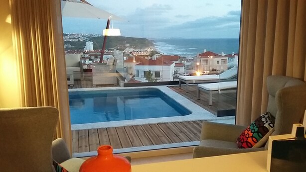 Une chambre avec vue sur une ville côtière, une piscine et une terrasse en bois.