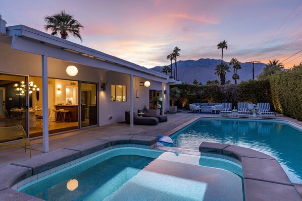 A modern house with a swimming pool, outdoor seating, and a mountain backdrop.
