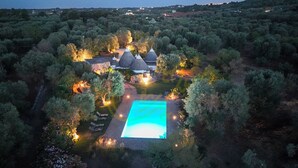 Eine Luftaufnahme einer Anlage mit Schwimmbecken, umgeben von Bäumen und einem Steinhaus mit einem Kegeldach.