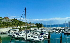 Un port de plaisance où sont amarrés de nombreux bateaux, un ciel bleu dégagé et une colline en arrière-plan, parsemée de bâtiments.