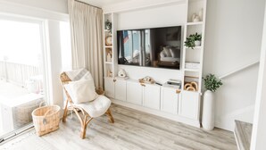 Ein Wohnzimmer mit einem weißen Fernseher, einem Korbsessel und einer weißen Schrank mit Regalen.