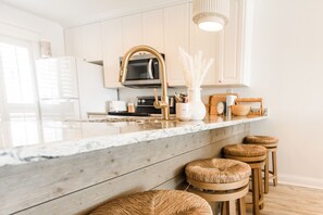 Une cuisine avec des armoires blanches, un plan de travail en bois, un robinet doré et trois tabourets en osier.