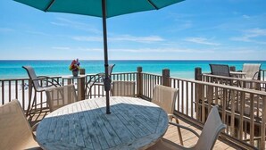 Eine Holzterrasse mit einem runden Tisch, Stühlen und einem Sonnenschirm, mit Blick auf das Meer.