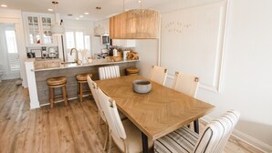 Eine moderne Küche mit einem Fischgrät-Holztisch, weißen Barhocker und einer hängenden Leuchte.