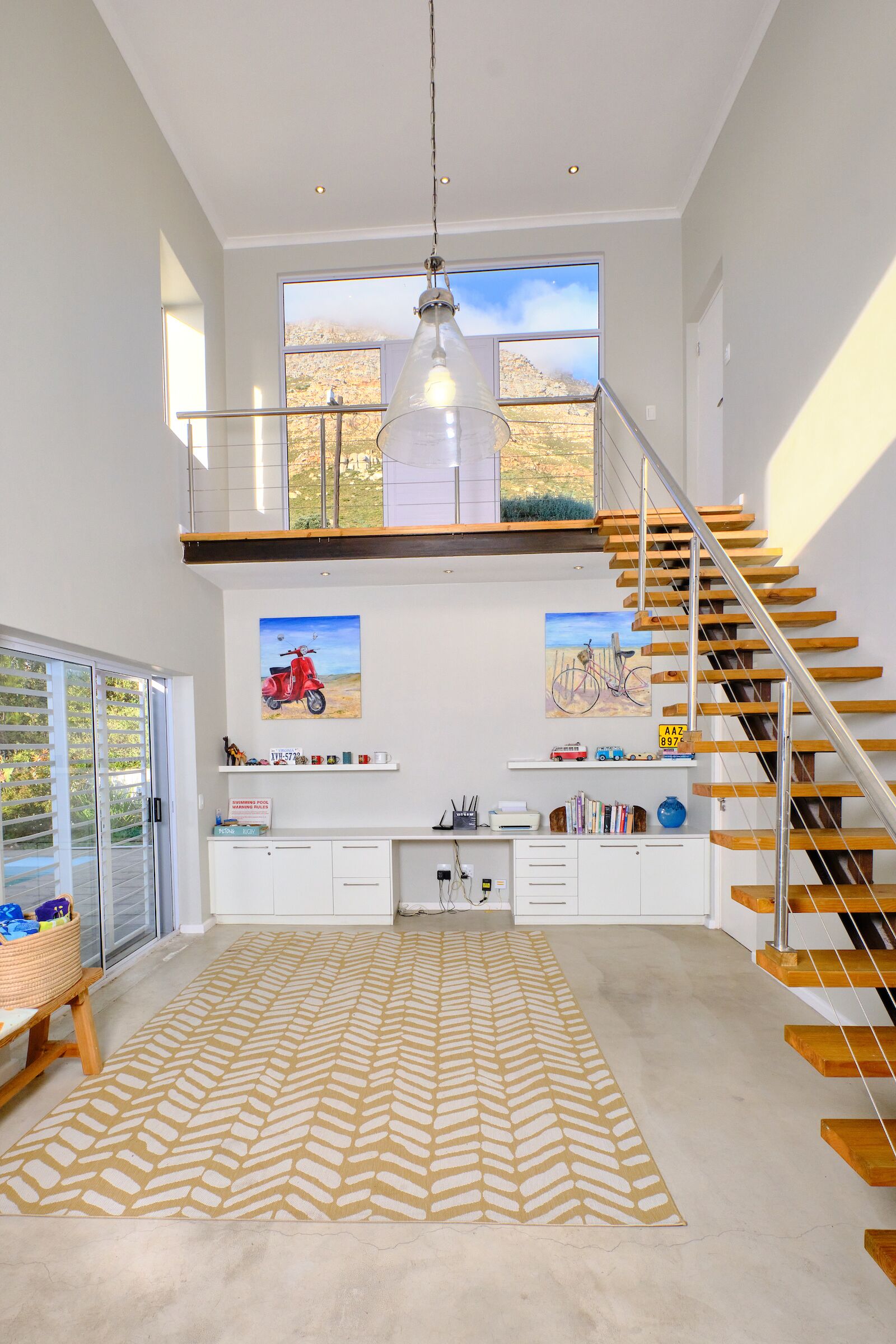 A spacious living area with a high ceiling, a staircase, and a large window overlooking a mountainous landscape.