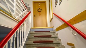 A staircase with red carpeted steps and white balusters, leading to a door with a wreath. - Ferienwohnung Greiz W2 (Greiz)