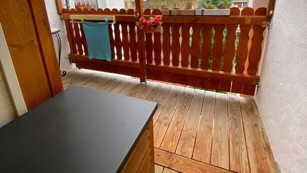 A wooden deck with a table, a wooden fence, and a view of buildings and a church steeple. - Ferienwohnung Greiz W2 (Greiz)