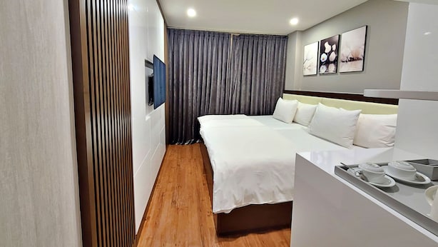A modern hotel room with a large bed, a bedside table with cups, a flat-screen TV, and a large window with curtains. - HANZ The Moon Hotel 2 (Ho Chi Minh City)