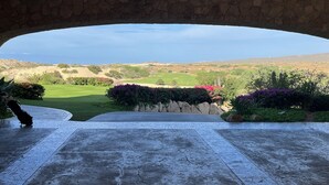 Vista desde un arco de piedra sobre un campo de golf con césped cuidado y cactus.