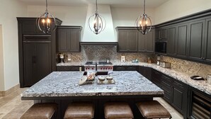 Una cocina moderna con armarios oscuros, una isla grande con taburetes, un tragaluz e iluminación colgante.