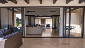 Un amplio salón con un gran ventanal corredera que da a un patio exterior, amueblado con un sofá, sillones y una mesa de comedor.