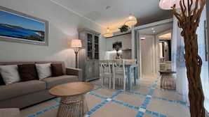 A living room with a sofa, a round coffee table, and a dining area with a table and chairs. There is a kitchen area with cabinets and a refrigerator.