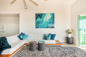 Un salon moderne avec un canapé blanc, des coussins turquoise, un tapis à poils longs gris et un grand tableau abstrait accroché au mur.