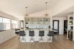 A modern kitchen with a central island, bar stools, and pendant lighting.