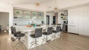 Una cucina moderna con isola centrale, sgabelli da bar e luci a sospensione.