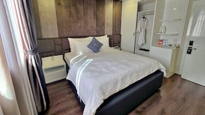 Habitació d'hotel moderna amb un llit gran, un armari, una taula de nit i un mirall.