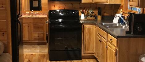 Et interiør af en træhytte med et køkken, der indeholder en komfur, mikroovn og træskabe.