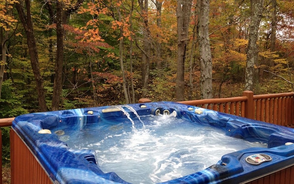 A hot tub surrounded by a wooden deck and autumn foliage.