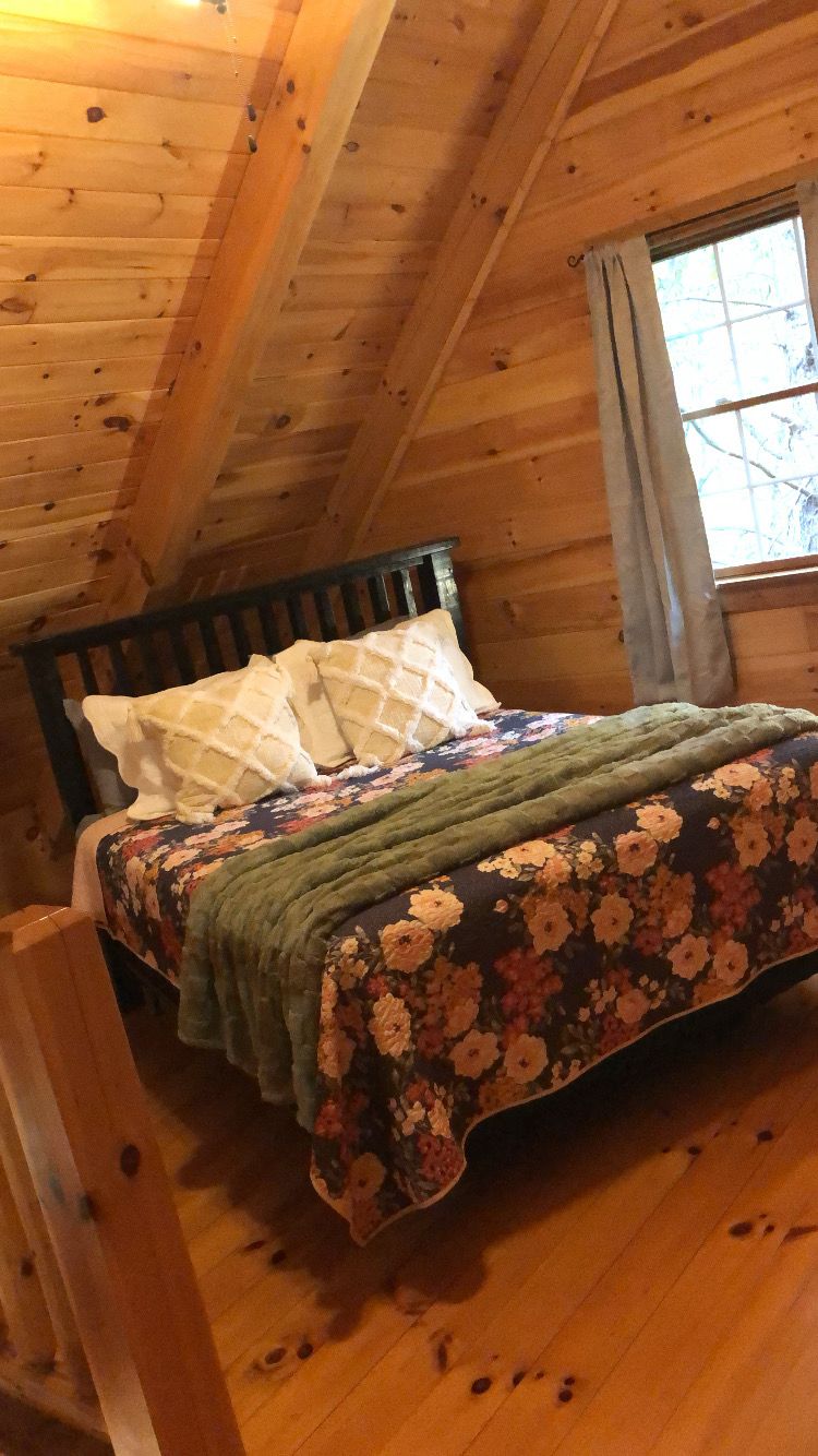 A wooden cabin bedroom with a bed, pillows, and a window.