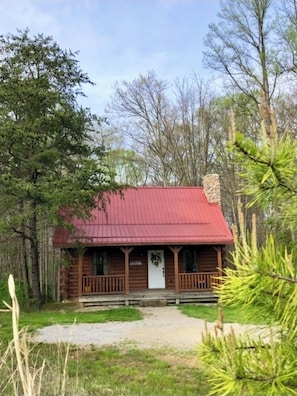 A rustic cabin with a red roof, wooden exterior, and a porch.