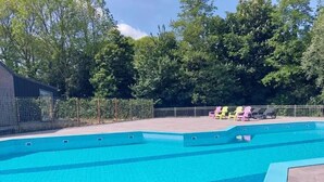 A swimming pool with a tiled deck area, surrounded by a fence and trees.
