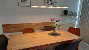 A dining area with a wooden table, four chairs, a vase with flowers, and a shelf with decorative items.