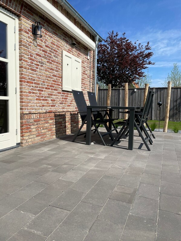 A patio with a brick wall, a wooden fence, and a table with chairs. - Luxury vacation home The Crab (Sint-Annaland)