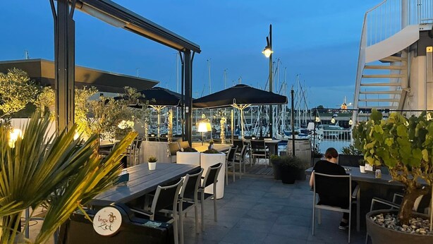 Un espace extérieur aménagé pour les repas, avec des tables, des chaises, des parasols et des plantes en pot.