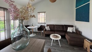 Un salon moderne avec un vase en verre rempli de fleurs, un canapé marron, une table basse ronde et une petite table d’appoint.