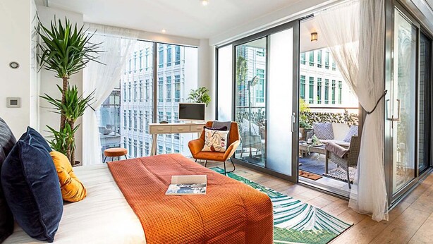Una habitación de hotel moderna con una cama, un escritorio, una silla y un balcón con vistas a la ciudad.